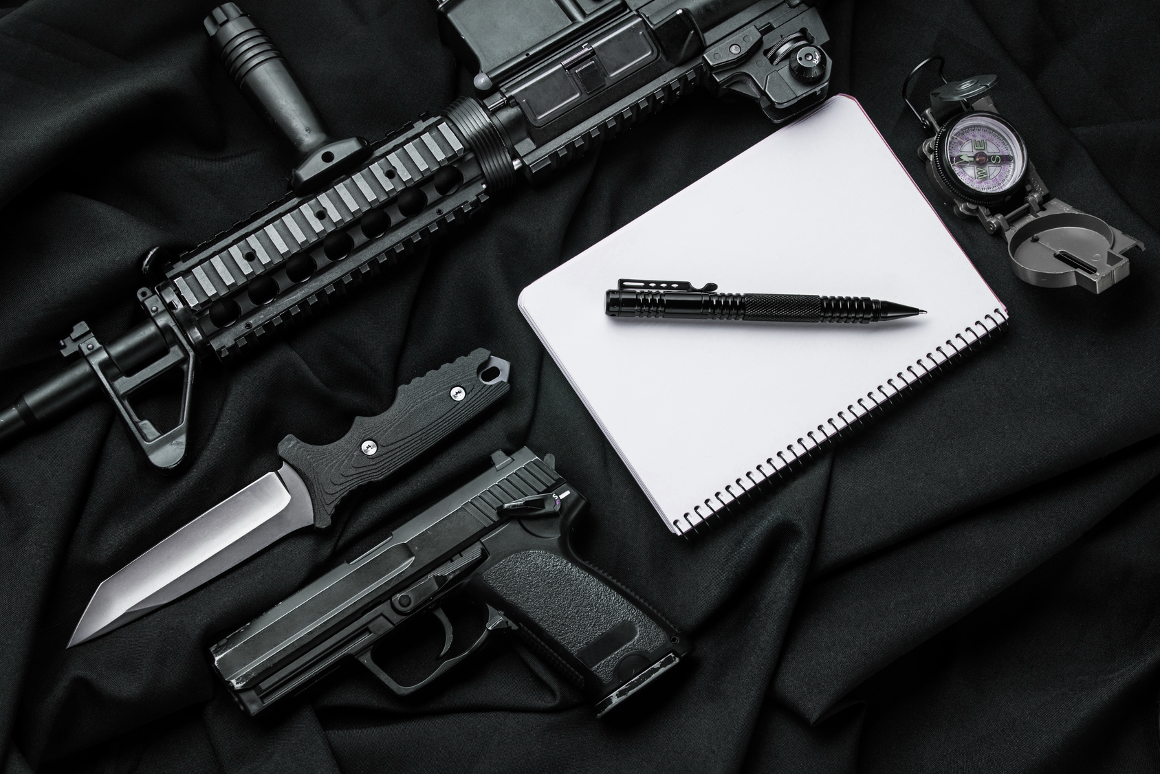 Кifle, pistol,  knife,  notebook with  pen and compass lying on black cloth. Top view