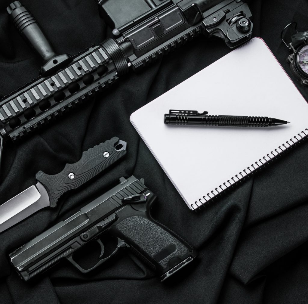 Кifle, pistol,  knife,  notebook with  pen and compass lying on black cloth. Top view